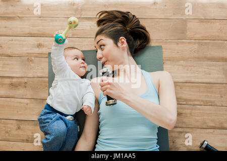 Draufsicht der Mutter mit Baby am Boden liegen und spielen mit Hanteln Stockfoto