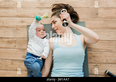 Draufsicht der Mutter mit Baby am Boden liegen und spielen mit Hanteln Stockfoto