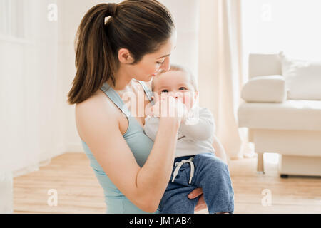 Porträt der schönen Mutter Kind an ihre Brust haltend und mit ihm spielen zu Hause Stockfoto