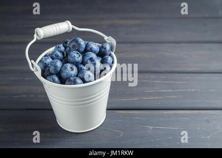 Heidelbeeren in Blecheimer weiß auf schwarzem Hintergrund aus Holz Stockfoto