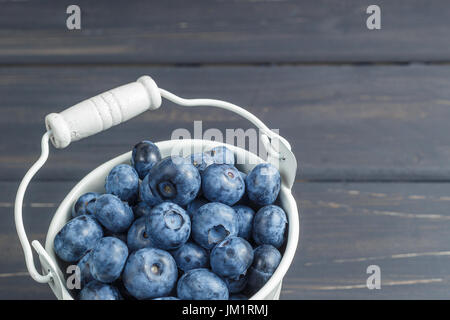 Heidelbeeren in Blecheimer weiß auf schwarzem Hintergrund aus Holz Stockfoto