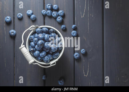 Heidelbeeren in Blecheimer weiß auf schwarzem Hintergrund aus Holz. Ansicht von oben Stockfoto