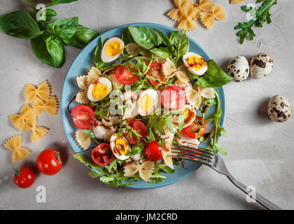 Farfalle-Fliege-Pasta-Salat mit Wachteleiern, Kirschtomaten, Rucola, Mozzarella und Basilikum, gekleidet mit Balsamico-Sauce über grauen Beton Hintergrund Stockfoto