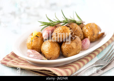 Ofen gebackene Kartoffeln oder Pellkartoffeln mit Rosmarin und Knoblauchzehen auf einem weißen Teller Stockfoto