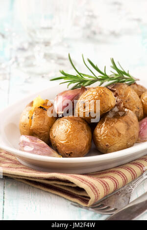 Homemeade gebackene Kartoffeln oder Jacken Kartoffeln mit Rosmarin und Knoblauchzehen auf weißen Teller Stockfoto