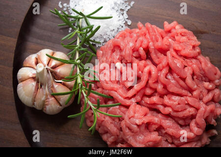 Hamburger Vorbereitung Zutaten. Rohes Hackfleisch mit Knoblauch und Rosemay am Holz Hintergrund. Stockfoto