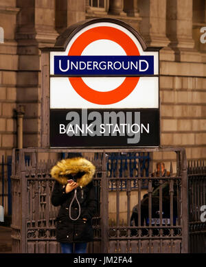 Nachtansicht der Bank Junction, stellen Menschen Blick auf ihr Handy. Bankenviertel, Bank-u-Bahnstation vorhanden. City of London. Stockfoto