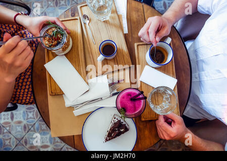 Paar von Mann und Frau am Tag Ihr Frühstück morgens im Café. Müsli, Schokolade Kuchen, Smoothie und heißen Kaffee auf dem Tisch. Flatlay, selektiven Fokus. Stockfoto