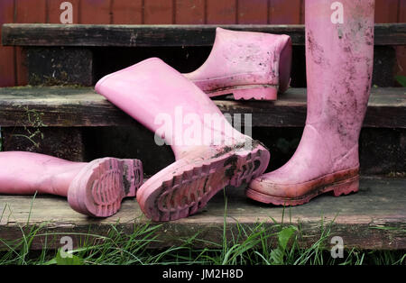Verlassene schmutzig rosa Gummistiefel auf der Holztreppe. Im freien zugeschnittenen Foto Stockfoto