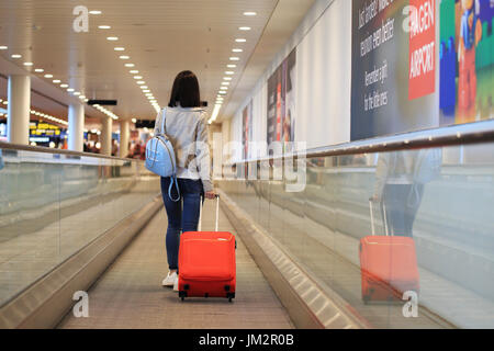 Flughafen von Kopenhagen, Dänemark - 15. Juli 2017: ein Mädchen mit roten Koffer auf Rolltreppe im Flughafen. Stockfoto