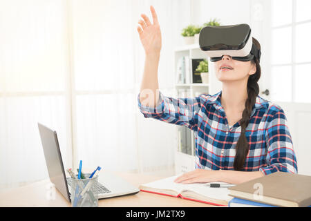 junge Frau mit einer virtual-Reality-Kopfhörer mit konzeptionellen Netzlinien verbinden Laptop Business Content und hand Geste in der Luft während der Arbeit im th Stockfoto