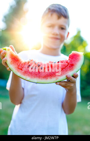 Kleiner Junge hält Wassermelone Slice in Outdoor-Sonnenuntergang Stockfoto