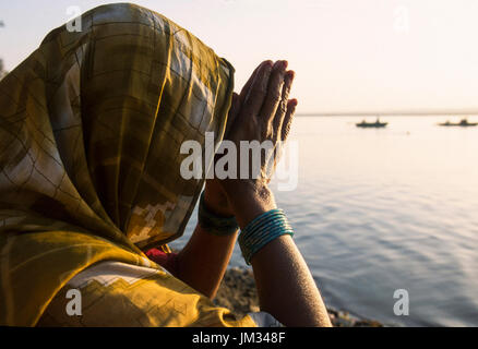 Indien, Uttar Pradesh, Varanasi, Hinduistische Frau Falten Hand für Morgengebet für Lord Shiva und Göttin Ganga bei Fluss Ganges, mit Blick auf den Sonnenaufgang, den alten Banaras oder Kashi oder ANANDAVANA (Wald von Bliss) ist ein heiliger Ort für die Hindus zu erreichen Moksha bedeutet Rettung vom ewigen Kreis der Wiedergeburt, die Ganga Fluss ist ein Übergang von der Erde zum Himmel, ein sehr religiöser Ort für Erleuchtung bliss Hingabe Reinigung Stockfoto