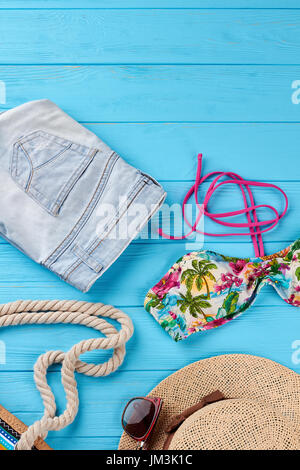 Einstellung des Strand-Accessoires. Gewebt, Hut, Jeans-Shorts, Sonnenbrille, BH, blaue Vintage-Hintergrund. Stockfoto