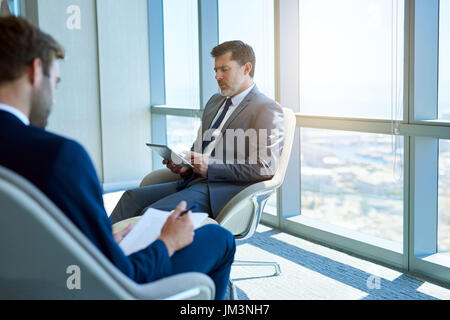 Reife Geschäftsmann lesen Informationen über ein digital-Tablette, mit jüngeren Geschäftsmann Informationen auf einem Formular ausfüllen Stockfoto