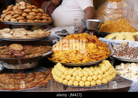 Haufen von Indische Süßigkeiten auf dem Display in einem Shop in Pushkar, Rajasthan, Indien. Rundlichen Körper des Inhabers sichtbar. Stockfoto