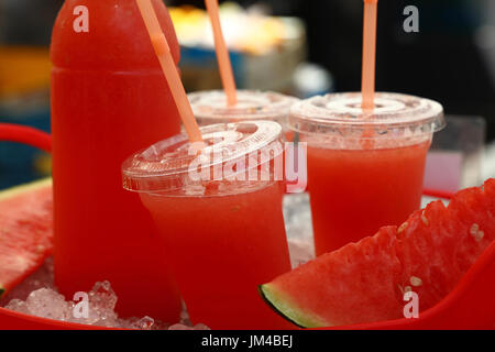 Frisch gepressten rote Reife Wassermelonensaft in Plastikbechern mit Strohhalmen und Flasche auf dem Eis im Retail Markt Stall Display, Nahaufnahme, niedrigen Winkel Stockfoto