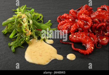 Meeresfrüchte, die kleinen ganz rot Baby-Oktopus-Salat mit grünen Algen und Erdnuss-sauce auf Schiefer Tafel, Nahaufnahme, hoher Winkel Stockfoto