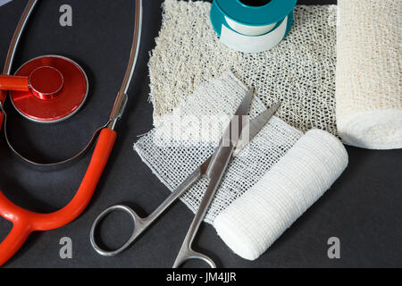 Medizinische Bandagen mit Schere, Heftpflaster und medizinische Stethoskop auf schwarzem Hintergrund. Medizinische Instrumente. Stockfoto