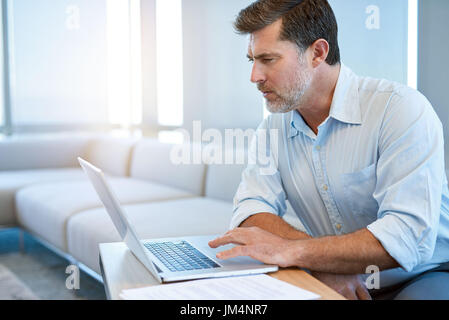 Schöne Reife Geschäftsmann in eine Business-Lounge sitzen arbeiten seine Laptop-Computer mit einem ernsten Ausdruck Stockfoto
