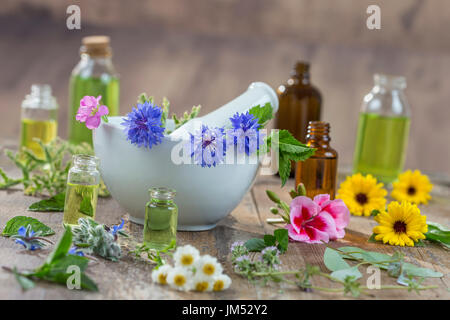 Ätherische Öle für die Aromatherapie Behandlung mit frischen Kräutern in Mörtel und wesentliche oik Flasche auf dem Rücken auf bleue Holzbrett Hintergrund Stockfoto