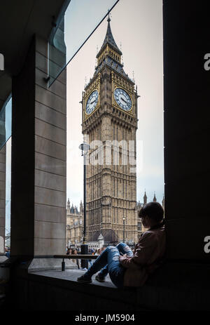 Eine junge Frau sitzt allein gegenüber der Londoner Big Ben Clock in Westminster, Großbritannien. Stockfoto