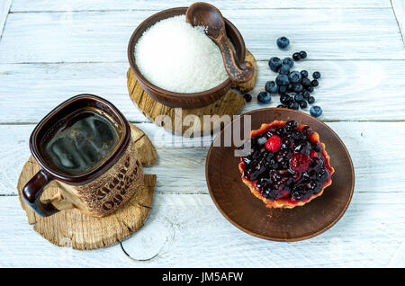 Tasse Kaffee und einem süßen Kuchen. Kuchen in einem Korb mit Beeren bestreut. Verschüttete Blaubeeren auf den Tisch. Stockfoto