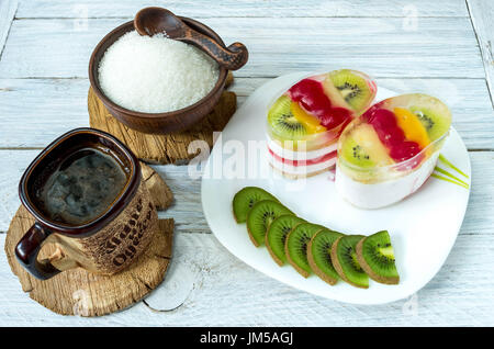 Portion Kaffee-Pause. Käsekuchen mit Obst-Scheiben und in Scheiben geschnittenen Kiwi. Kaffee auf dem Tisch. Stockfoto