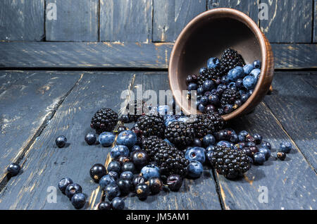 Zusammensetzung von Waldbeeren. Beeren sind von der Platte verteilt. Die Beeren sind von dunkler Farbe. Beeren auf einem dunklen Hintergrund. Stockfoto