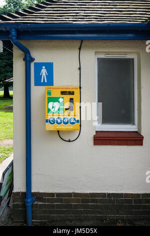 Defibrillator montiert an der Wand eines männlichen öffentlichen connvenience Toilette in Harrogate, North Yorkshire, England, UK. Stockfoto