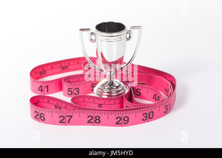 Verliert Gewicht oder Fitness Erfolgskonzept mit Silber Champion Sport Cup und rot oder rosa Maßband auf weiße Fläche Stockfoto
