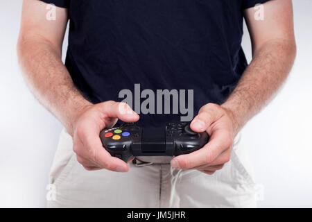 Hände des erwachsenen Mannes spielen Videospiele, auf weißen Sofa sitzend mit Joystick Controller in haarigen Händen tragen schwarzes T-shirt. Zugeschnittenes Bild betrachtet aus Stockfoto