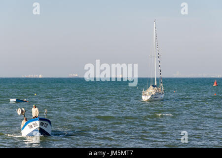 Fischer in kleinen Boot nähert sich der Küste mit paar große Schiffe im Hintergrund, Pomorie, Bulgarien Stockfoto