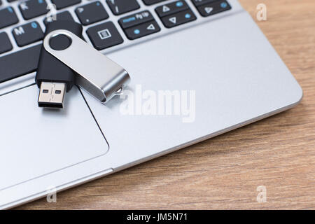 Abnehmbaren USB-Stick oder Flash-Laufwerk auf einer offenen Laptop-Computer in eine Nahaufnahme seitlichem Blick von oben auf einem hölzernen Tisch liegend Stockfoto