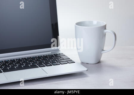 Kaffee Pause am Arbeitsplatz oder während des Studiums mit einem generischen weiße Becher neben einem Laptop-Computer in einer Nahaufnahme Stockfoto