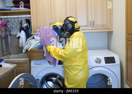 Reife Frau in gelb Haz-Mat Suir und Gasmaske sortieren Wäsche im Hause Zimmer. Stockfoto