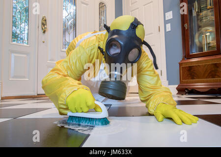 Reife Frau in gelb Haz-Mat Suir und Gasmaske auf Boden schrubben schwarzen und weiße Fliesen. Stockfoto