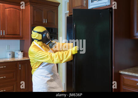 Reife Frau in gelb Haz-Mat Suir und Gasmaske, die Kühlschranktür zu öffnen, in der Küche zu Hause. Stockfoto