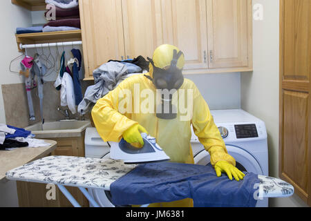 Reife Frau in gelb Haz-Mat Suir und Gasmaske Bügeln Hemd an Bord mit Dampfbügeleisen. Stockfoto