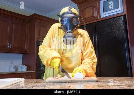 Reife Frau in gelb Haz-Mat Suir und Gasmaske hacken Zwiebeln in Küche zu Hause. Stockfoto