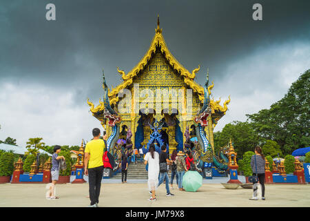 Chiang Rai, Thailand - 12. Juli 2017: Unbekannte Menschen stehen in der Nähe von Sanctuary in Wat Rong Sua Ten oder blau Tempel bei Regen Wolken Hintergrund. Stockfoto