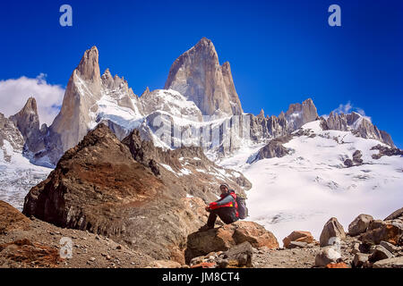 Männliche Trekker ruht auf den Felsen vor der atemberaubenden und beeindruckenden Mount Fitz Roy in der Nähe von El Chalten in Patagonien, Argentinien Stockfoto