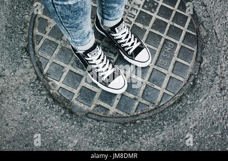 Sankt-Petersburg, Russland-30. Mai 2017: Teenager Füße in einem Paar von schwarzem Canvas Freizeitschuhe Chuck Taylor All-Stars auf städtischen Kanaldeckel stehen Stockfoto