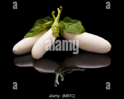 Drei weiße Auberginen mit Wassertropfen und grüne Blätter isoliert auf Schwarz mit echten Reflexion Stockfoto