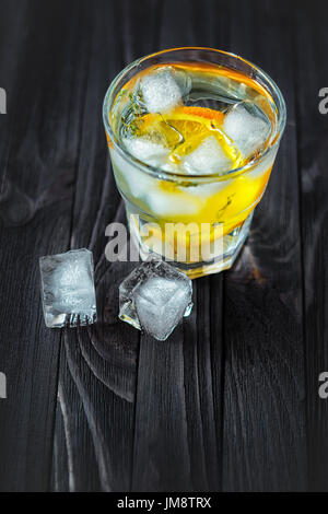 Ein erfrischendes Getränk mit Orange, Würfel aus Eis und Rosmarin in einem Glas auf einem Tisch aus dunklem Holz. Stillleben in ein Restaurant oder eine bar Stockfoto
