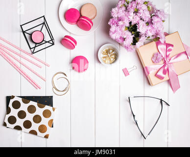 Rosa Blüten, Macarons, Kerze, Gläser und andere niedliche kleine feminine Accessoires auf dem weißen Holztisch Stockfoto