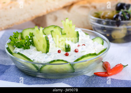 Frischen griechischen Tzatziki mit Knoblauch und Gurken, Brot und Oliven im Hintergrund Stockfoto