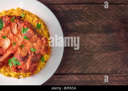 Eine Nahaufnahme von Osso Buco, traditionelles italienisches Gericht serviert mit Risotto Alla Milanese, Safranreis und Gremolata, geschossen von oben auf eine dunkle rustikale tex Stockfoto