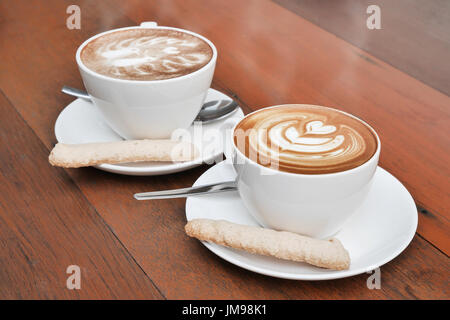 zwei Tassen Latte Art Kaffee in eine weiße Tasse auf hölzernen Hintergrund Stockfoto