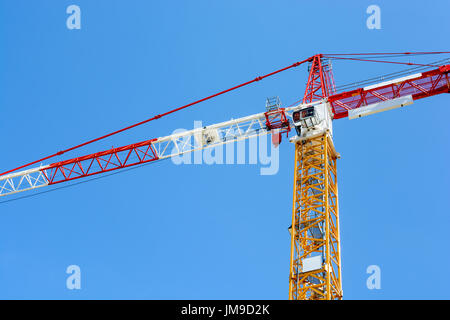 Niedrigen Winkel Blick auf ein Turmdrehkran mit gelben Turmteil und einem roten und weißen Ausleger und Gegenausleger Abschnitte gegen blauen Himmel. Stockfoto
